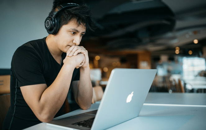 A man wearing headphones looking concerened at his laptop.