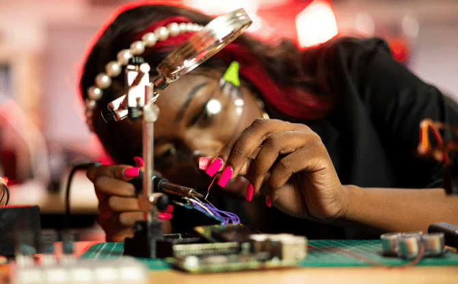 A woman with a pear headband and safety goggles soldering tech.