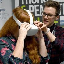 A man helping a girl with red hair use a VR headset.