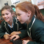 Two young girls in school uniform looking at a computer screen.