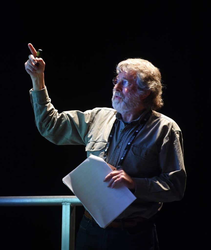 An older gentleman lit up on stage, pointing at the ceiling.