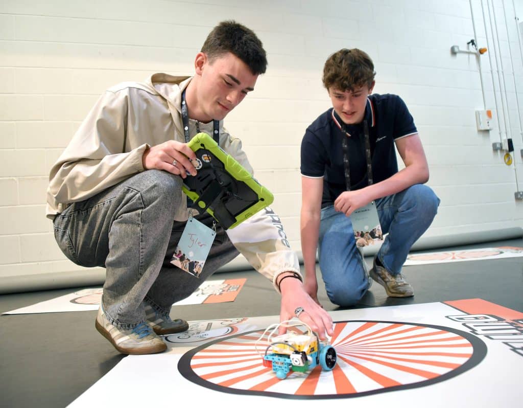 Two young men using a robot at Agile on the Beach youth.