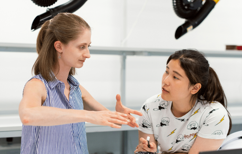 A woman talking to a young woman explaining with her hands how something works.